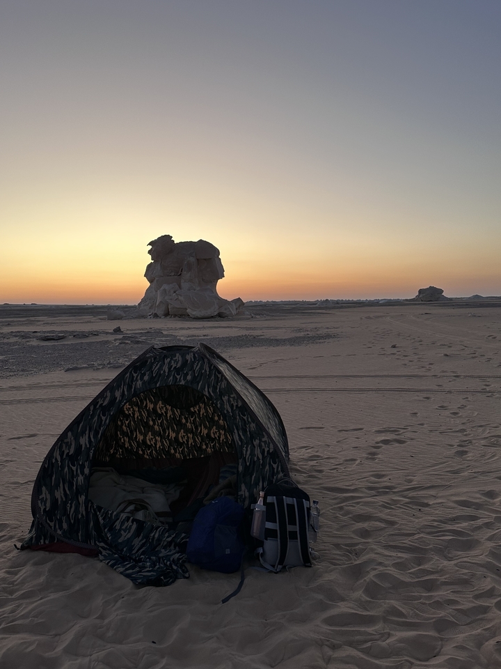 Une tente dans le désert au coucher du soleil avec des formations rocheuses.