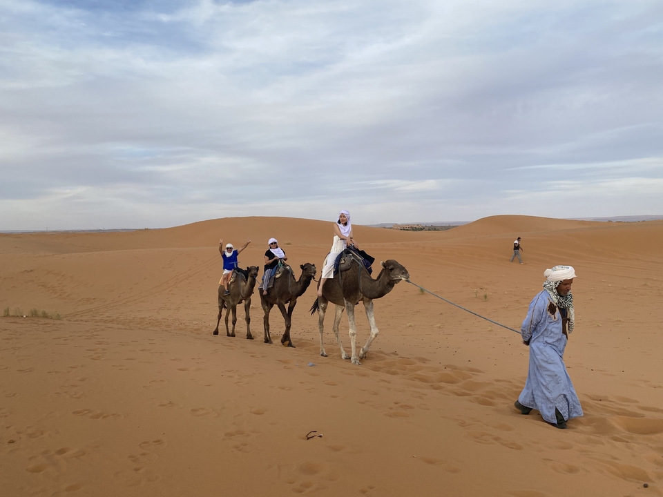 Des touristes chevauchant des chameaux à travers les dunes du désert menés par un guide.
