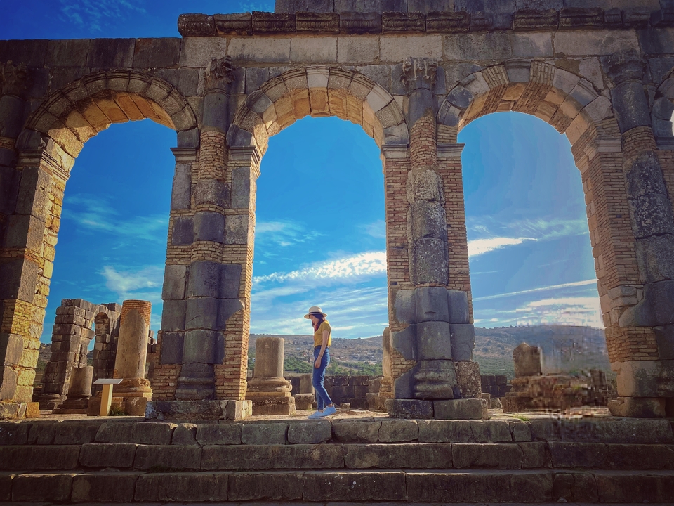 Une personne marchant à travers d'anciennes arches de pierre sous un ciel bleu.