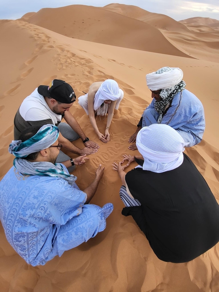 Groupe de personnes en tenue traditionnelle écrivant « Maroc » dans le sable.