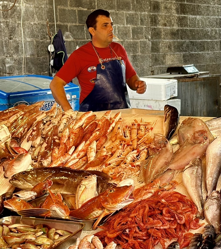 Un étal de marché avec une variété de fruits de mer frais et un vendeur.