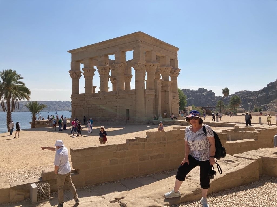 Ruines de temple avec visiteurs près d'une rivière dans un paysage désertique ensoleillé.