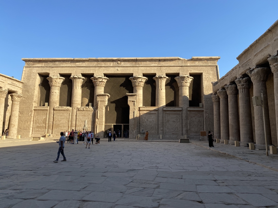 Cour de temple avec colonnes et des gens qui marchent.
