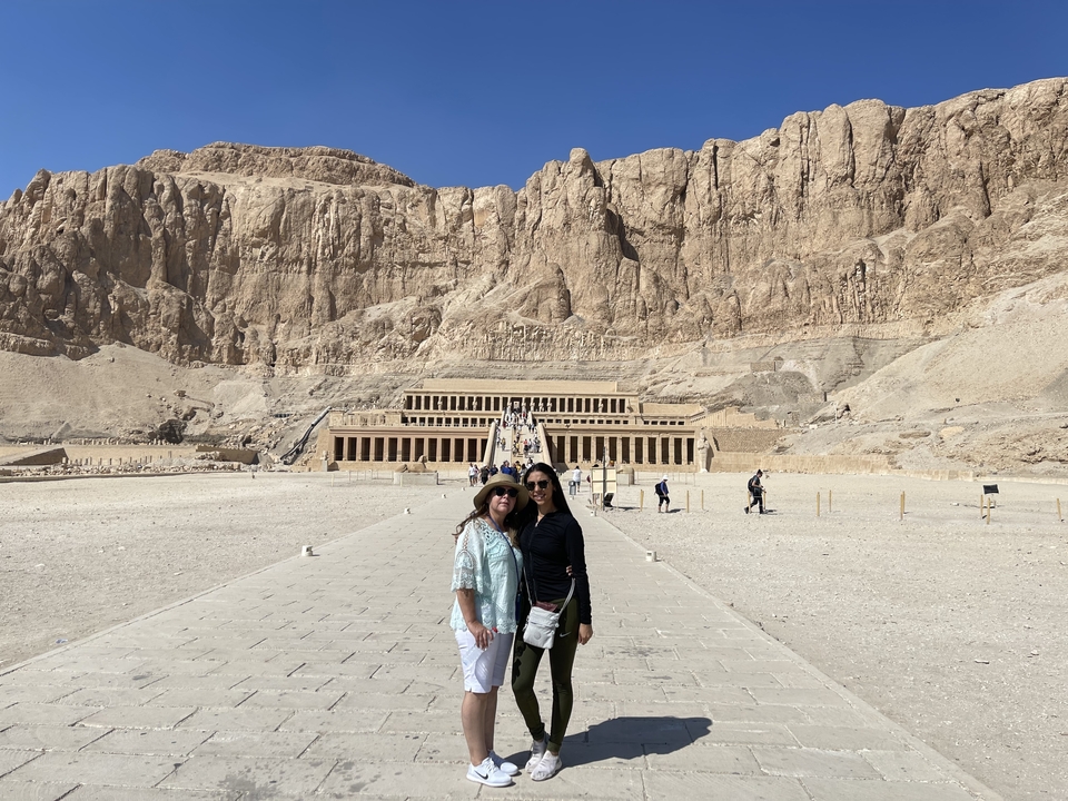 Deux personnes devant un vaste temple antique contre des falaises.