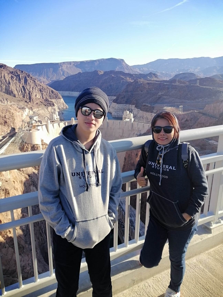 Des touristes posant avec un grand barrage en arrière-plan.