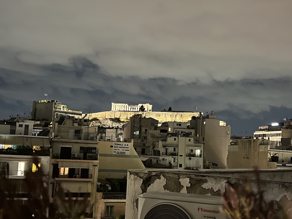 Vue nocturne de l'Acropole illuminée avec les bâtiments de la ville environnante.