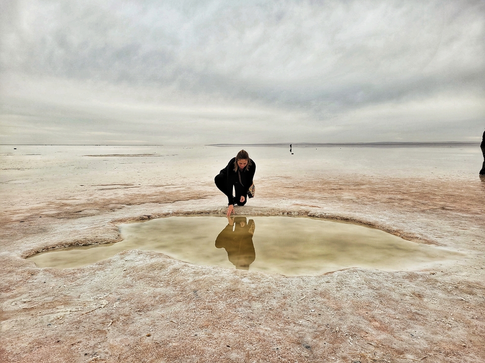 Personne agenouillée près d'un bassin d'eau réfléchissante sur un paysage plat.