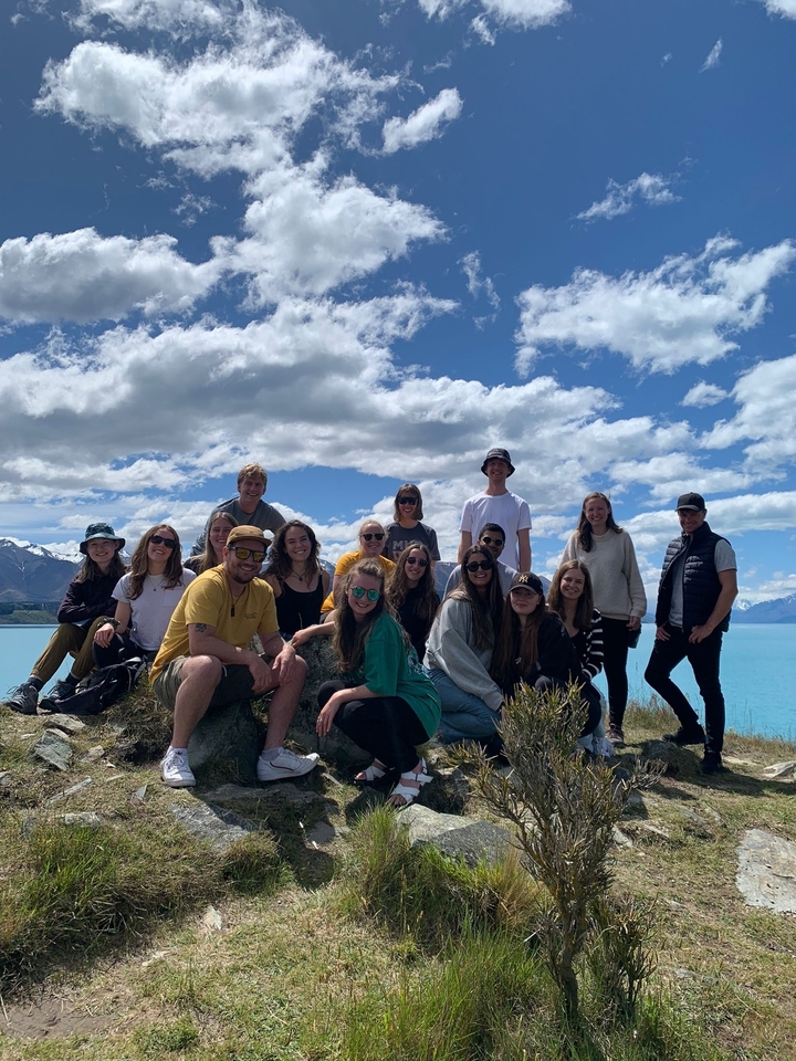 Friends gathered by a lakeside with mountains in the background.
