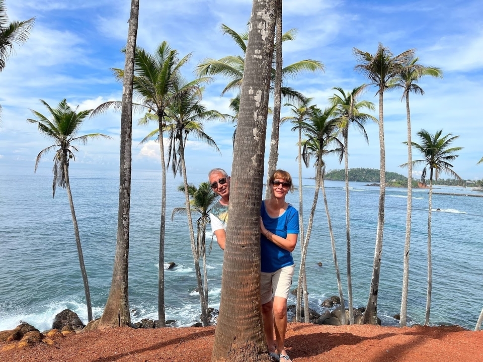 Deux personnes posant derrière un palmier près d'une plage tropicale.