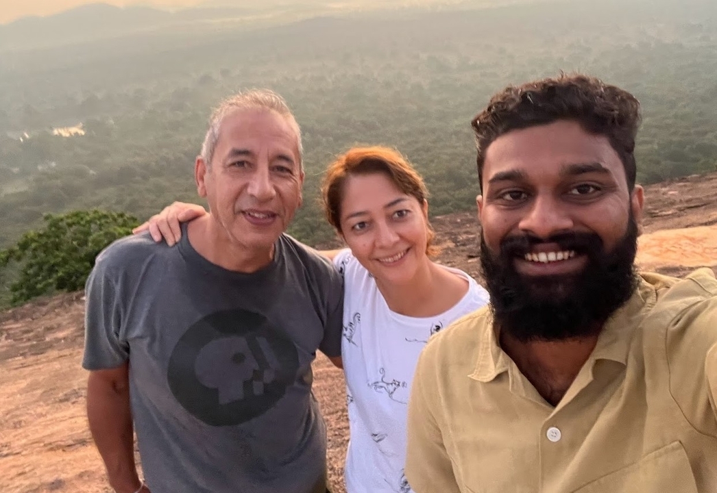 Trois personnes souriantes avec un paysage naturel en arrière-plan, possiblement pendant le coucher du soleil.