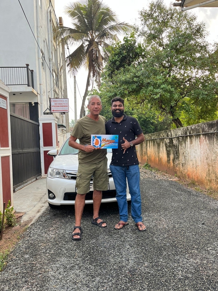Deux personnes posant avec un panneau près d'une voiture garée, à côté d'un bâtiment.