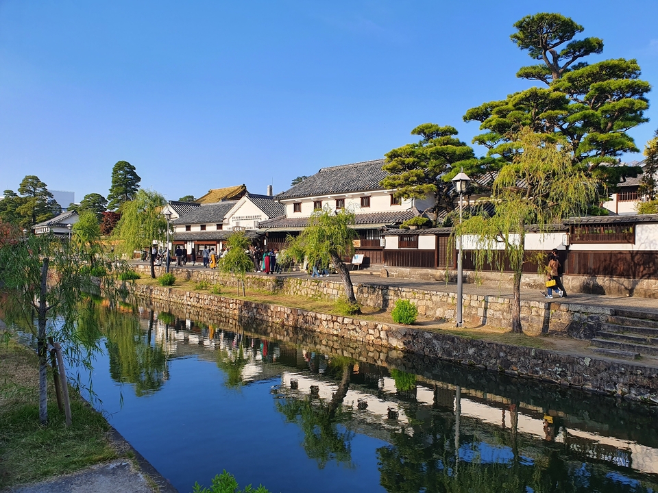Bâtiments japonais traditionnels reflétés dans un canal avec des arbres en surplomb.