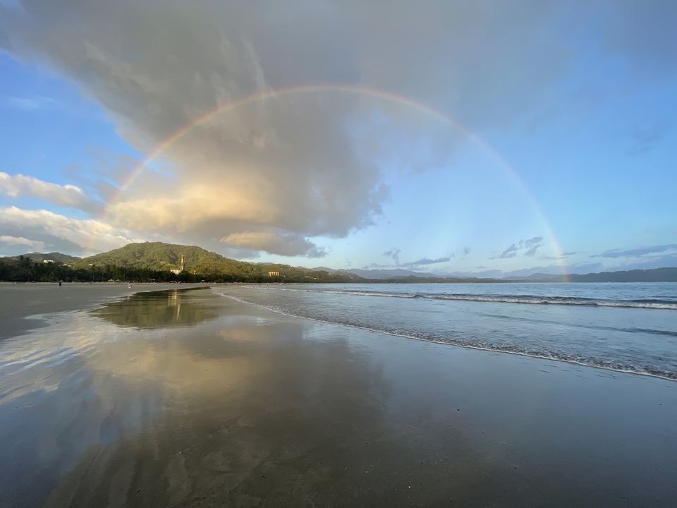 Arc-en-ciel au-dessus d'une plage sereine avec des eaux calmes et un ciel nuageux.
