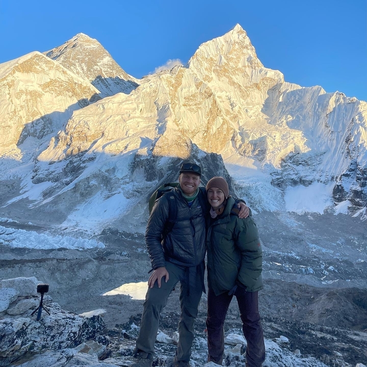 Couple souriant devant un paysage de montagne enneigée.