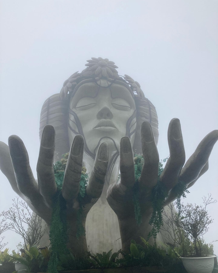 Grande sculpture de main tenant un visage serein par temps brumeux.