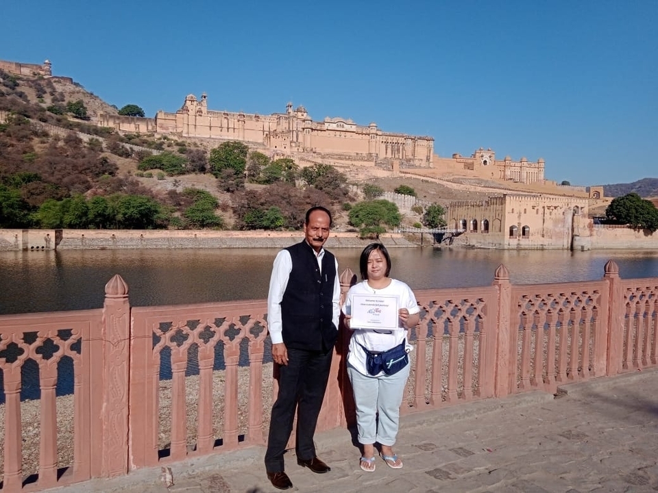 Deux personnes posant devant un grand fort rose de l'autre côté d'un lac.
