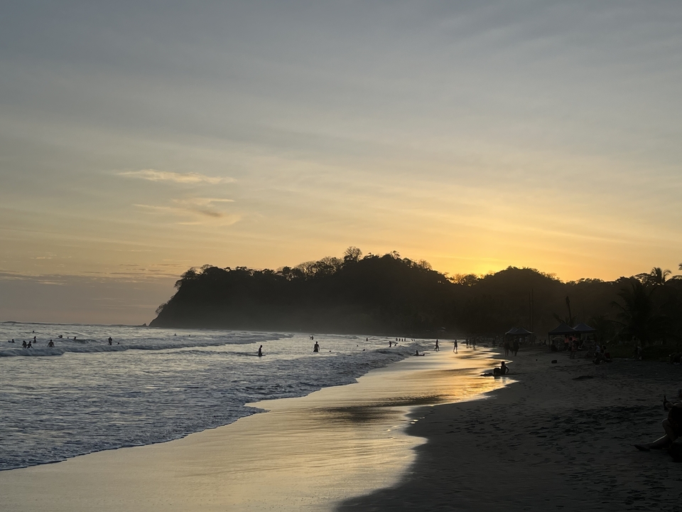 Scène de plage au coucher du soleil avec des gens profitant des vagues.