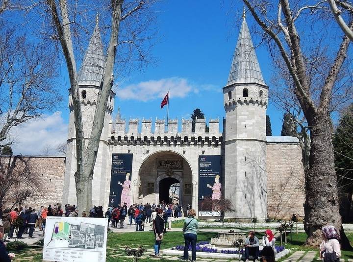 Grande porte en pierre avec tourelles et des gens qui la traversent à pied.