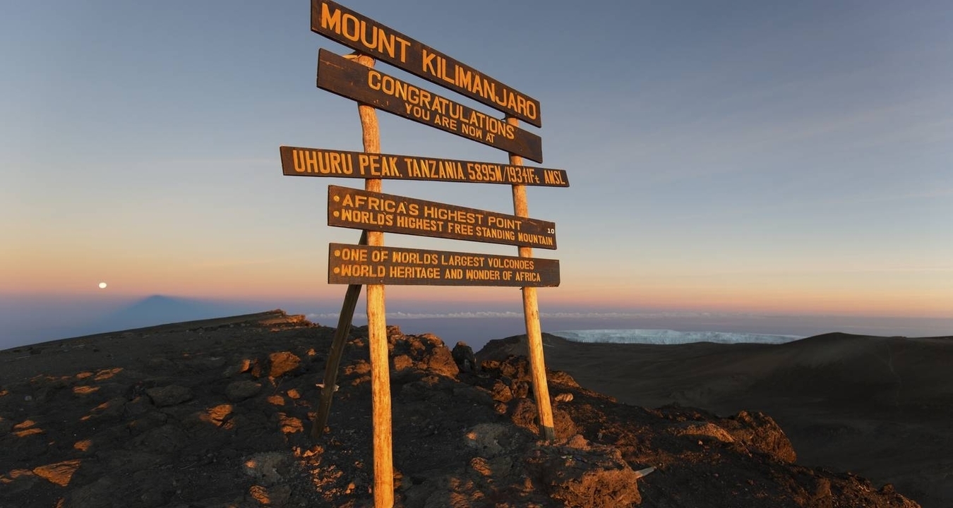 Vista del letrero del Monte Kilimanjaro al amanecer con una cordillera de fondo.