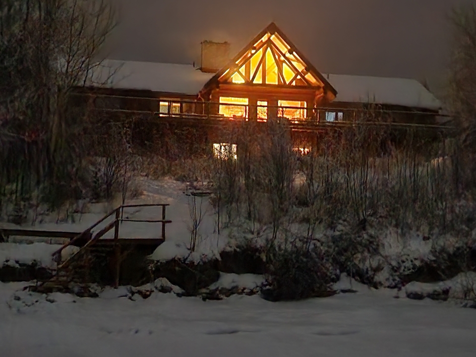 Une cabane en rondins éclairée de l'intérieur, située dans un environnement enneigé la nuit.