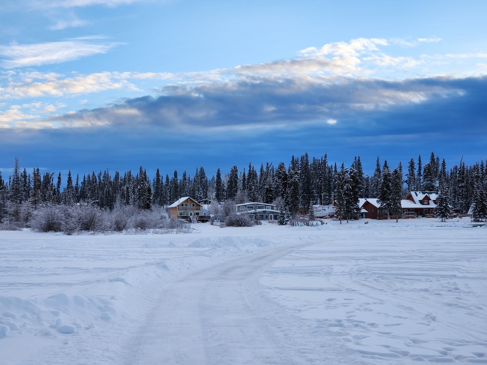 Paysage enneigé avec des maisons et des arbres sur un fond de ciel bleu nuageux.