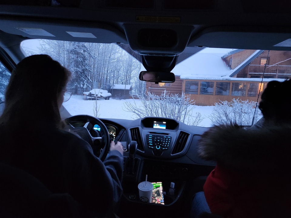 Intérieur d'un véhicule avec deux personnes à l'intérieur, garé devant un chalet couvert de neige.