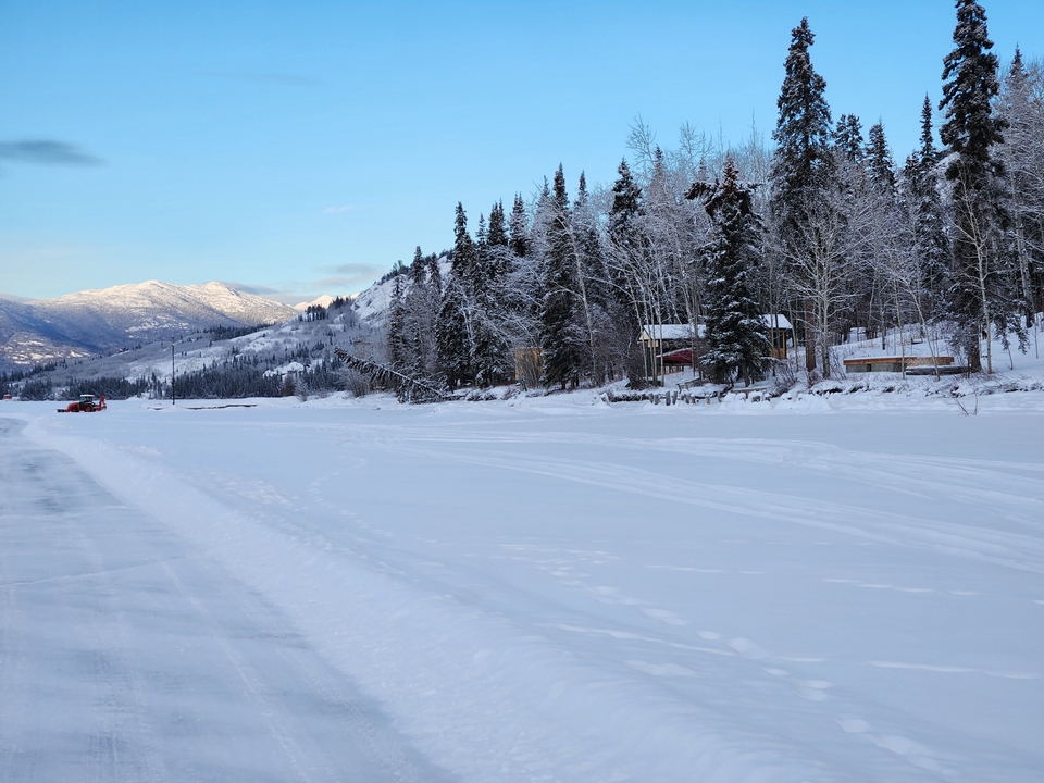 Un paysage d'hiver avec un terrain enneigé, des arbres et des montagnes enneigées au loin.