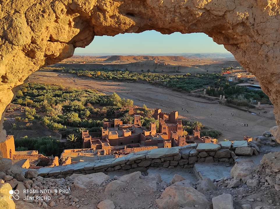Ait Benhaddou viewed through a natural rock window with a scenic landscape.