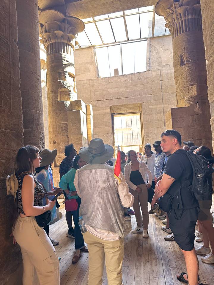 Groupe de touristes à l'intérieur d'un temple antique avec des colonnes et la lumière du soleil qui filtre.