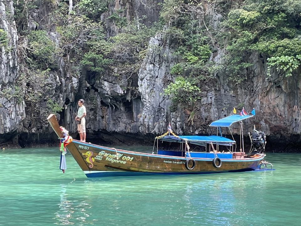 Bateau à longue queue dans des eaux turquoise cristallines près d'un rivage rocheux.
