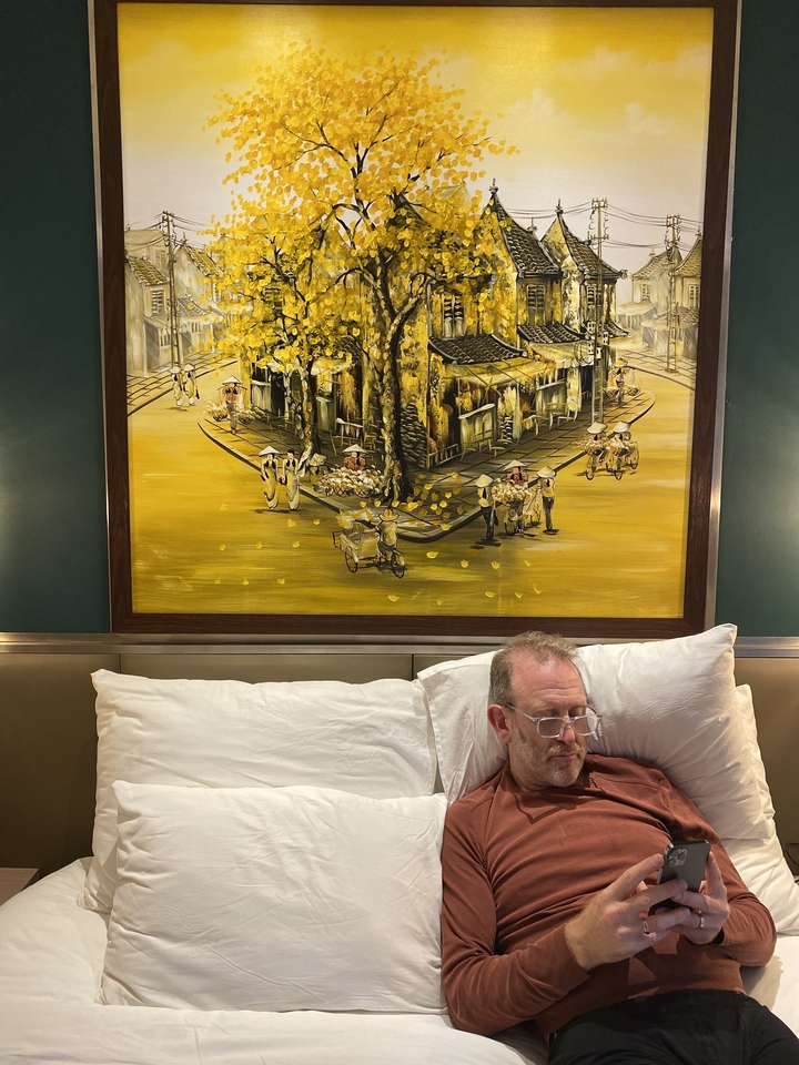 Homme assis sur un lit avec une grande peinture en arrière-plan.