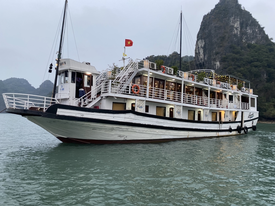 Bateau de croisière avec des lumières, sur une eau calme, avec des collines à l'arrière-plan.