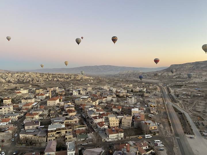 Montgolfières volant au-dessus d'une vallée avec des bâtiments au lever du soleil.