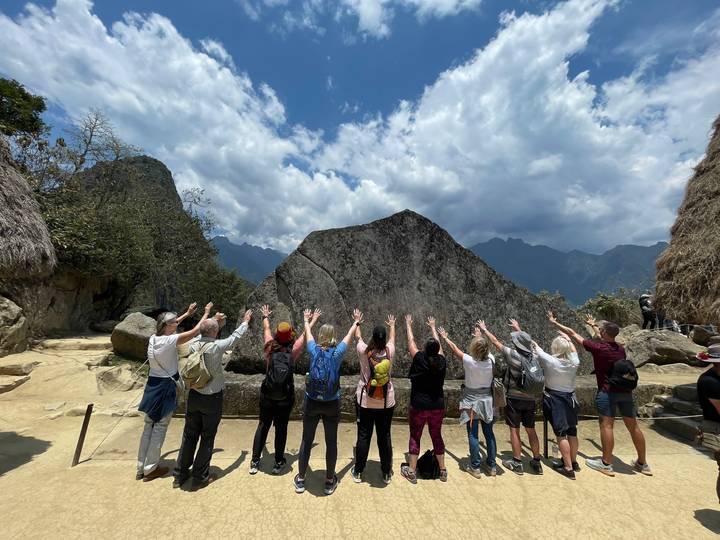 Group raising hands towards a large rock at Machu Picchu.