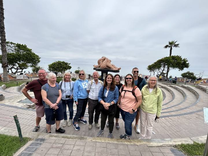 Group of people posing in a public space with a sculpture and trees.
