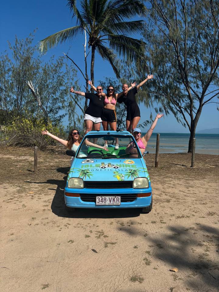 Des gens posent avec une voiture décapotable sur une plage.