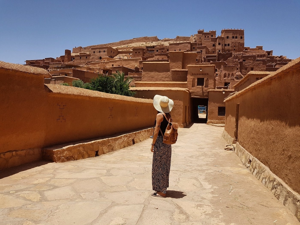 Person mit Sonnenhut, die durch eine antike Stadt im Adobe-Stil geht.