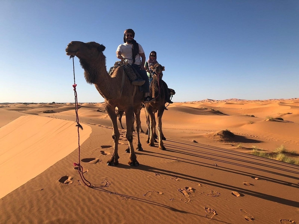 Zwei Menschen reiten auf Kamelen in einer Wüste bei klarem Himmel.