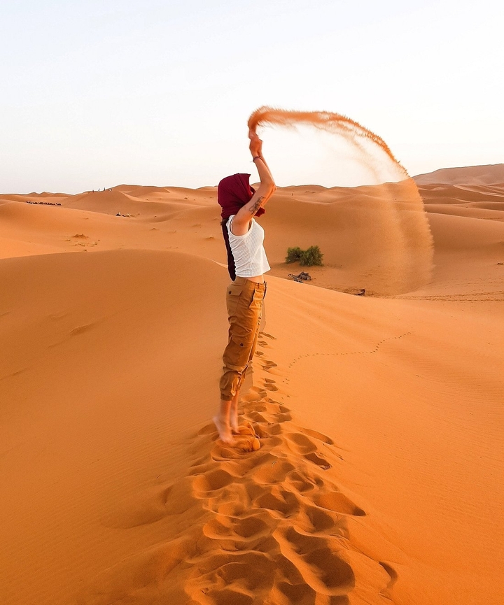 Person, die mit Sand in einer Wüstenlandschaft spielt.