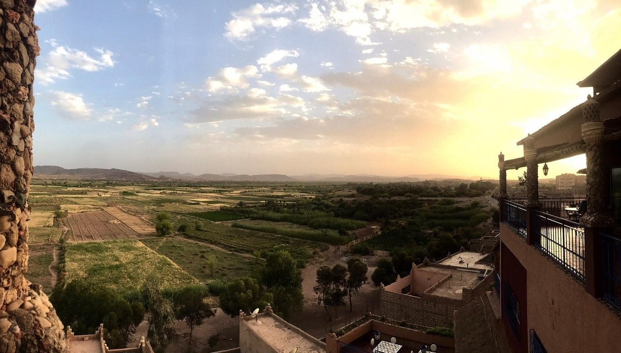 Luftaufnahme einer weiten grünen Landschaft mit fernen Bergen und Sonnenuntergang.