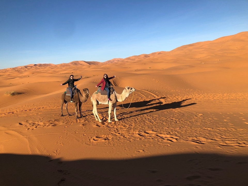 Zwei Menschen reiten auf Kamelen in einer sandigen Wüste.