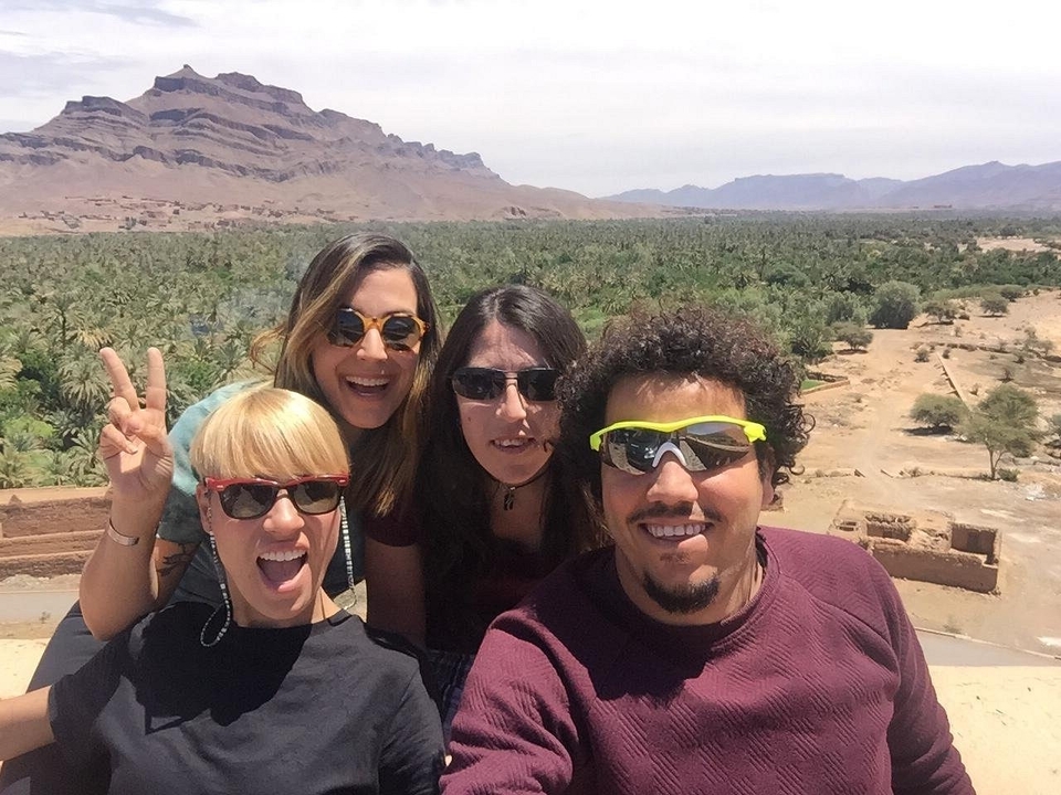 Eine Gruppe von vier Personen, die mit einer Wüstenlandschaft im Hintergrund posiert.