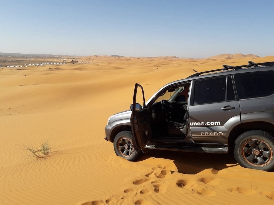 Ein Fahrzeug in der Wüste mit Sanddünen im Hintergrund.