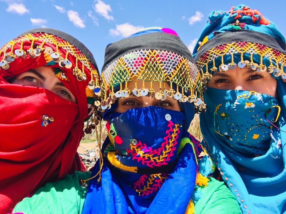 Drei Frauen in lebendiger Kleidung mit Wüstenlandschaft.