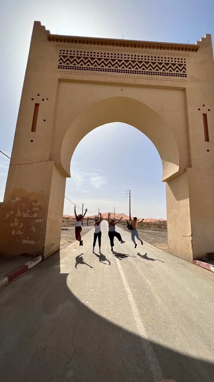 Gruppe von Menschen, die unter einem Bogen springen, mit offener Straße und Wüste dahinter.