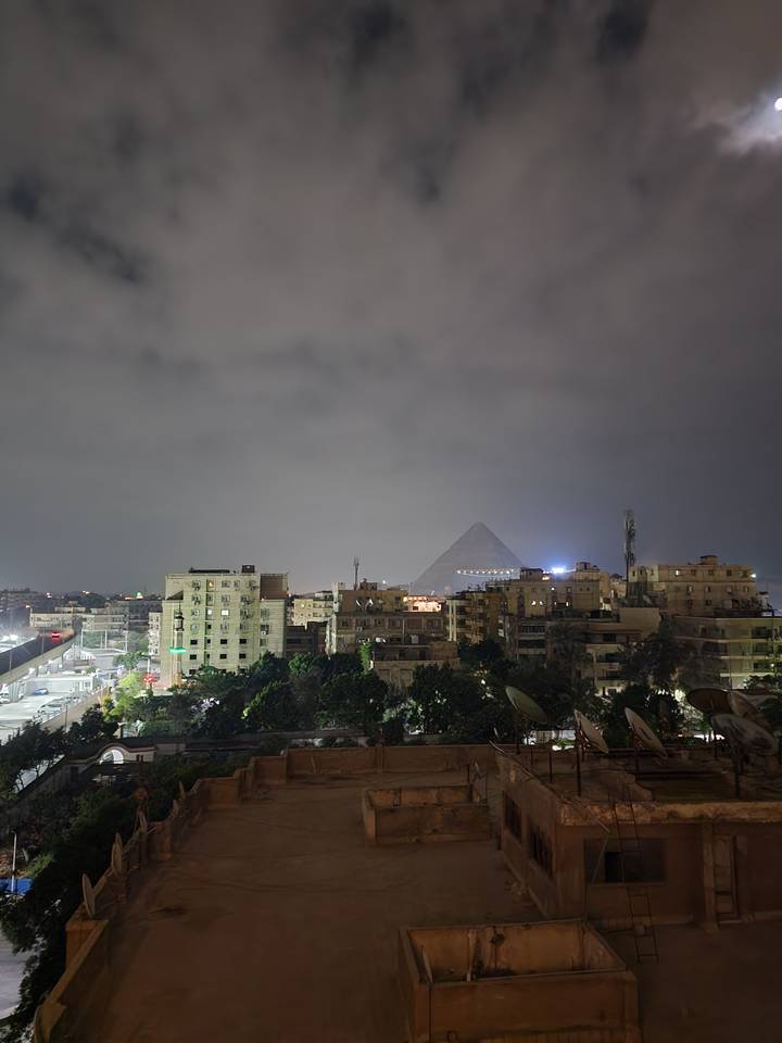 Vue nocturne d'un paysage urbain avec une pyramide en arrière-plan.