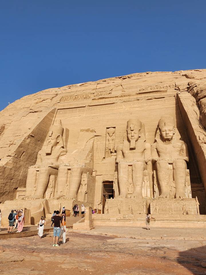 Grande façade de temple avec des statues sculptées dans la roche, des gens se promènent autour.