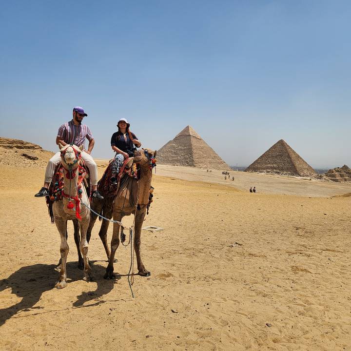Des gens à dos de chameau avec des pyramides en arrière-plan.