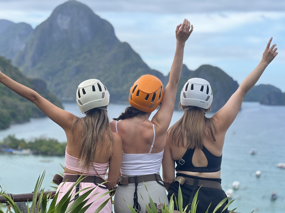Three individuals with helmets looking at a scenic bay view.