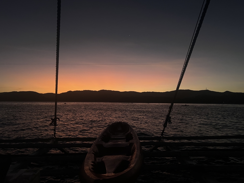 A silhouette of a boat on calm water during sunset.